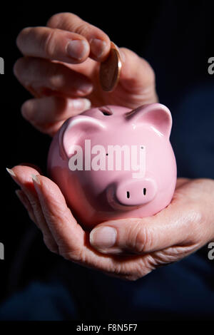 Senior woman saving money putting a coin inside piggy bank with a happy ...