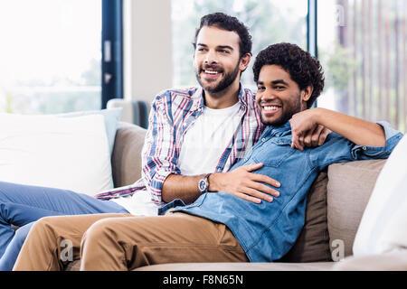 Smiling gay couple sitting on sofa Stock Photo