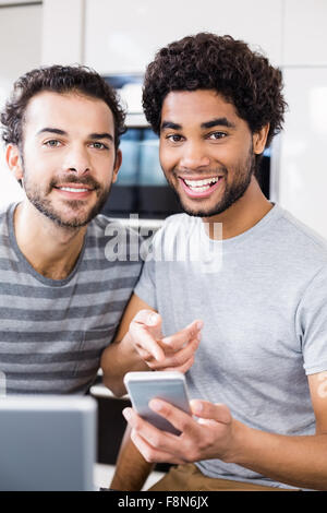 Smiling gay couple using smartphone in kitchen Stock Photo