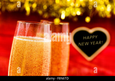 closeup of two glasses with champagne and a heart-shaped blackboard in the background with the text happy new year Stock Photo