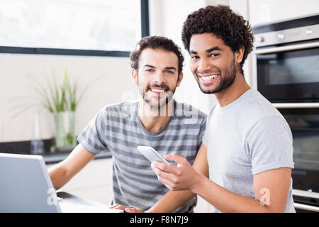 Happy gay couple using technology in kitchen Stock Photo