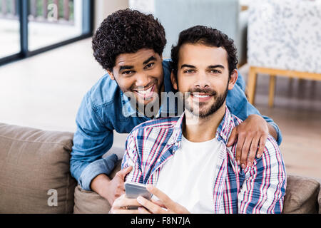 Happy gay couple using smartphone on sofa Stock Photo
