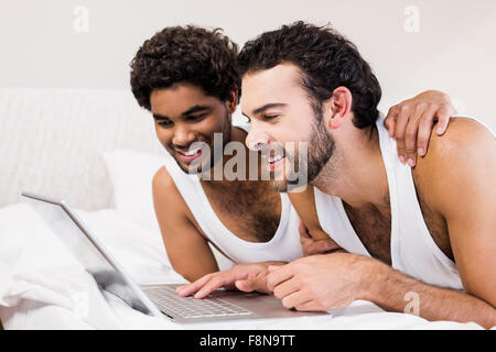 Happy gay couple laying on bed using laptop Stock Photo