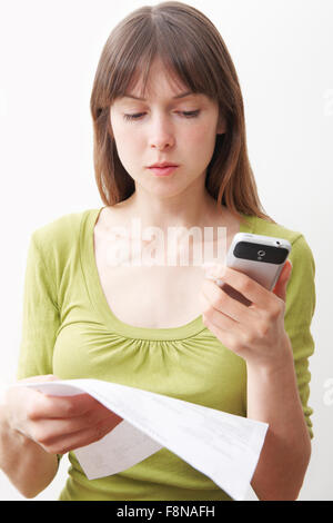 Young Woman With Mobile Phone And Bill Looking Worried Stock Photo