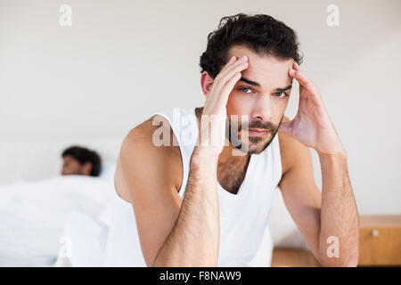 Troubled man sitting on bed in foreground Stock Photo