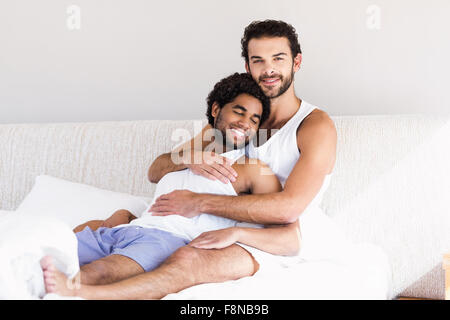 Smiling gay couple hugging on bed Stock Photo