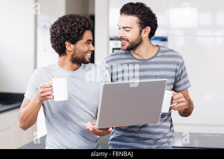 Happy gay couple using laptop and holding cups Stock Photo