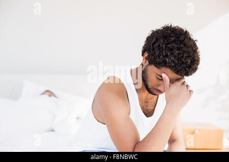 Troubled man sitting on bed in foreground Stock Photo