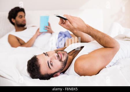 Smiling man using smartphone while partner reading book in background Stock Photo