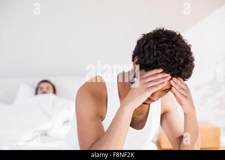 Troubled man sitting on bed in foreground Stock Photo