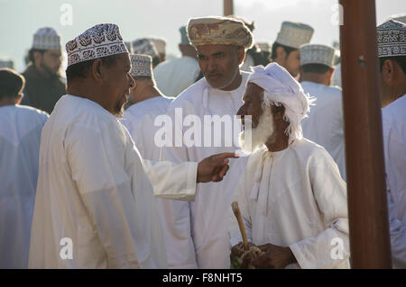 Three men chat at the lively Thursday livestock market in Nizwa, Oman Stock Photo