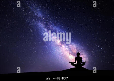 Milky Way. Night sky with stars and silhouette of a woman practicing yoga. Stock Photo