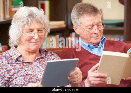 Senior Couple Using Digital Tablet And Reading Book Stock Photo