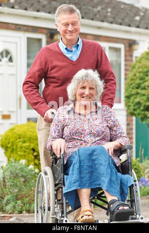 Senior Man Pushing Disabled Wife In Wheelchair Stock Photo
