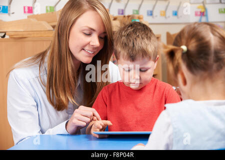 Teacher Helping Elementary School Pupil Use Digital Tablet Stock Photo