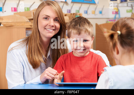 Teacher Helping Elementary School Pupil Use Digital Tablet Stock Photo