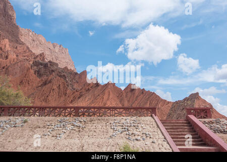 Stairs leading up to red mountain on a sunny day with white clouds Stock Photo