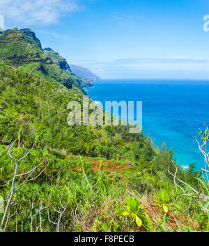 Sweeping view of the Na Pali Coast on Kauai, with hiker admiring views on the Kalalau Trail as kayakers explore the sea Stock Photo
