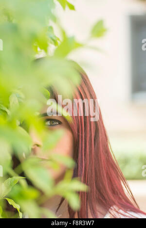 Young woman peeking through the leaves outdoors Stock Photo