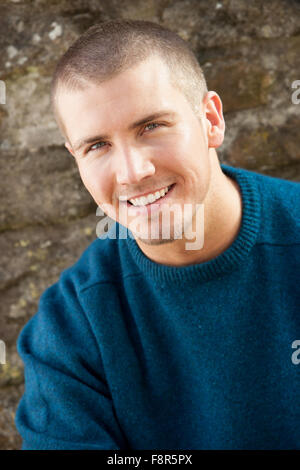 Attractive young man sitting outside. He is smiling at the camera. Stock Photo