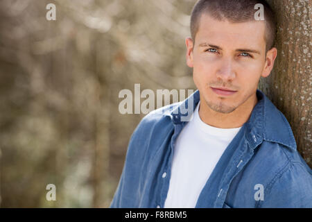Close up shot of an attractive young man leaning against a tree outdoors Stock Photo