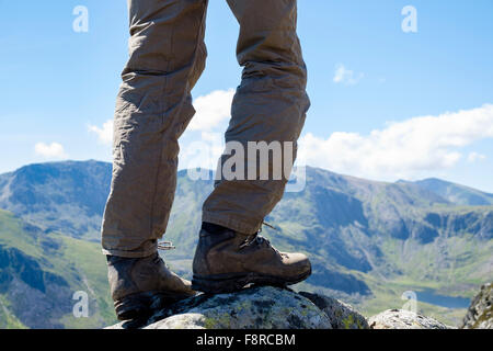 Hiker's legs wearing walking boots hiking on Carnedd Pen yr Ole Wen with view to Glyders and Snowdon in distance. Snowdonia National Park Wales UK Stock Photo