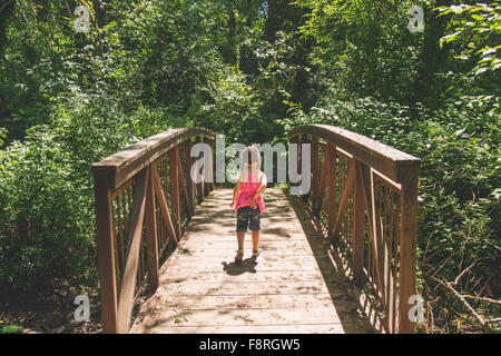 Young girl walking across bridge in woods Stock Photo