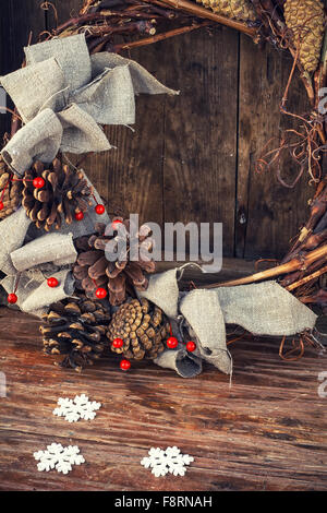 Woven from twigs and decorated with pine cones Christmas wreath on wooden background. Stock Photo