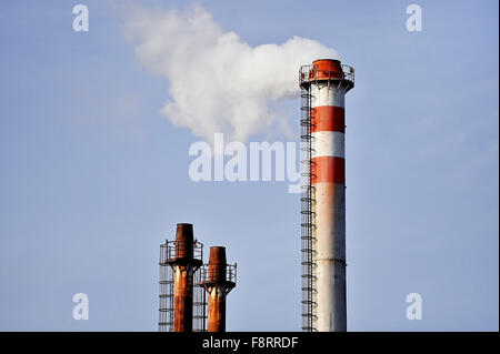 Smoke and steam coming out from an industrial petrochemical plant chimney with a blue sky on the background Stock Photo