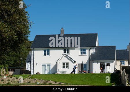 A man mowing his lawn outside a new 'executive' style detached house on a suburban private housing estate development on the outskirts of Aberystwyth Wales UK Stock Photo