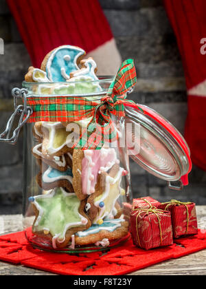 Assorted Christmas gingerbread cookies with colorful icing in glass jar on table Stock Photo