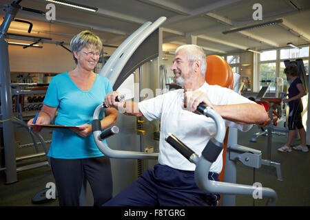 Fitness trainer explaining rowing machine in gym Stock Photo