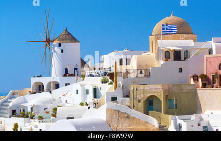 Santorini landscape with white houses, windmill and greek flag - Oia Town,  Santorini Island, Cyclades, Greece Stock Photo
