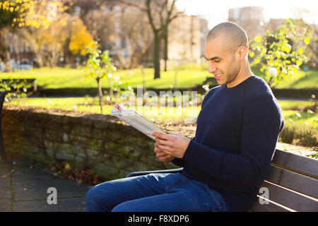 Young man sitting on a park bench reading a magazine Stock Photo