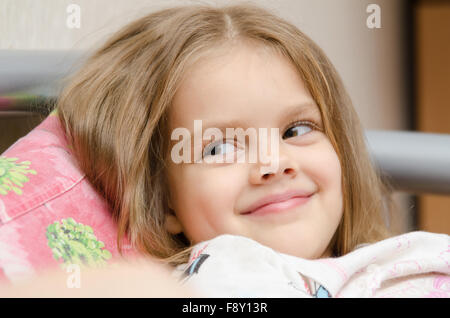 Cheerful five year old girl lying on the bed and looked left smorit Stock Photo