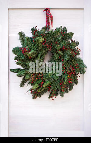 Green Christmas wreath hanging on white wooden door Stock Photo