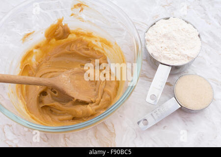 Measuring cups of flour and sugar with a peanut butter mixture in a glass bowl Stock Photo