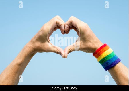 Gay athlete making hand heart with gay pride rainbow colors wristband against bright blue sky Stock Photo