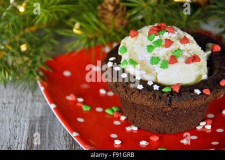 Christmas candy sprinkles on vanilla ice cream in brownie cup on red plate with holiday decorations. Stock Photo