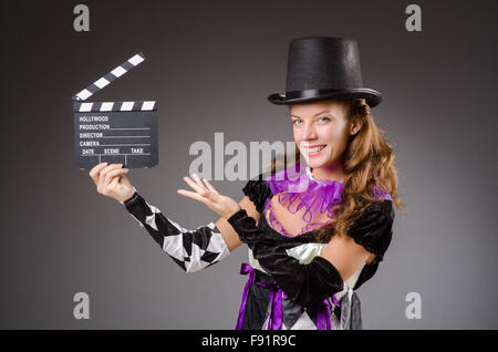 Pretty girl in jester costume holding clapperboard against gray Stock Photo
