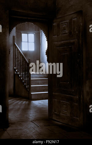 Wooden door leading to a dark room with window revealing high levels of light Stock Photo