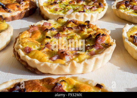 Assortment of quiche lorraine tartlets on wooden board, hand made with bacon and eggs Stock Photo