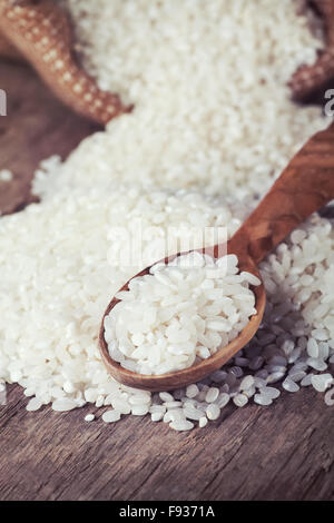 White rice spill out of the burlap bag and wooden spoon on the wooden table Stock Photo
