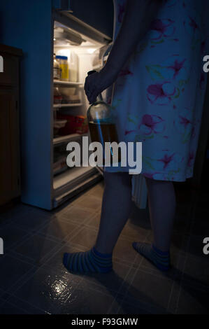 Woman opening refrigerator door at night to get a snack holding a bottle Stock Photo