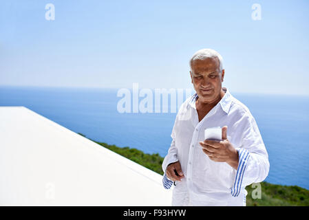 senior man using smart phone outdoor with ocean view background Stock Photo