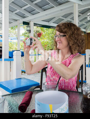 A 50 year old Caucasian woman takes a picture with her smart phone at a beachside cafe in St. Croix, U.S. Virgin Islands. Stock Photo