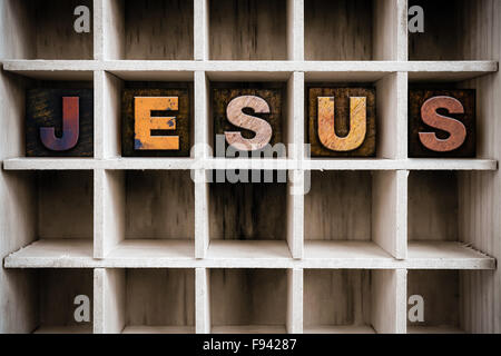 The word 'JESUS' written in vintage ink stained wooden letterpress type in a partitioned printer's drawer. Stock Photo