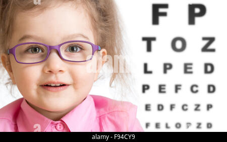 Smiling girl putting on glasses with blurry eye chart behind her Stock Photo
