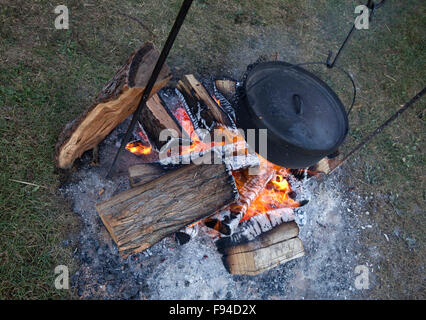 Cast iron Dutch oven hanging over a campfire to cook food. Stock Photo