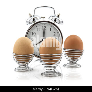 Three Eggs in egg cups with old clock on white background Stock Photo